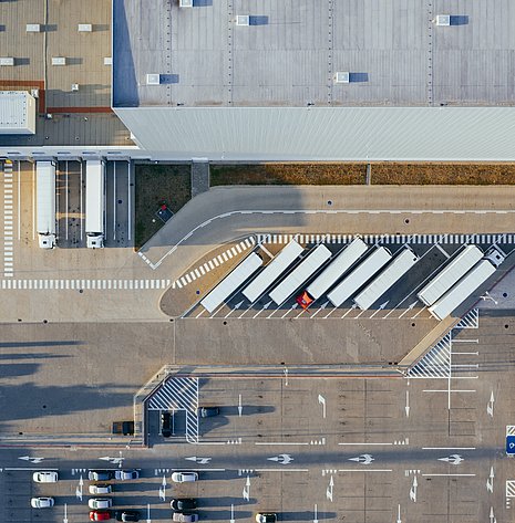 Bird's eye view of logistics facility, fleet of trucks and logistics hall can be seen.