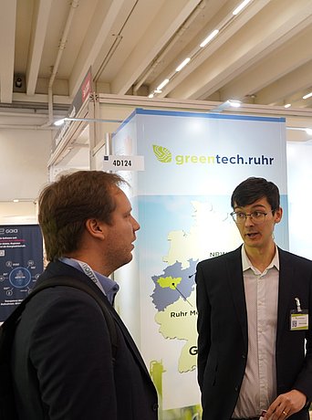 Zwei Messebesucher unterhalten sich am Stand von Greentech.Ruhr auf der E-world 2024.