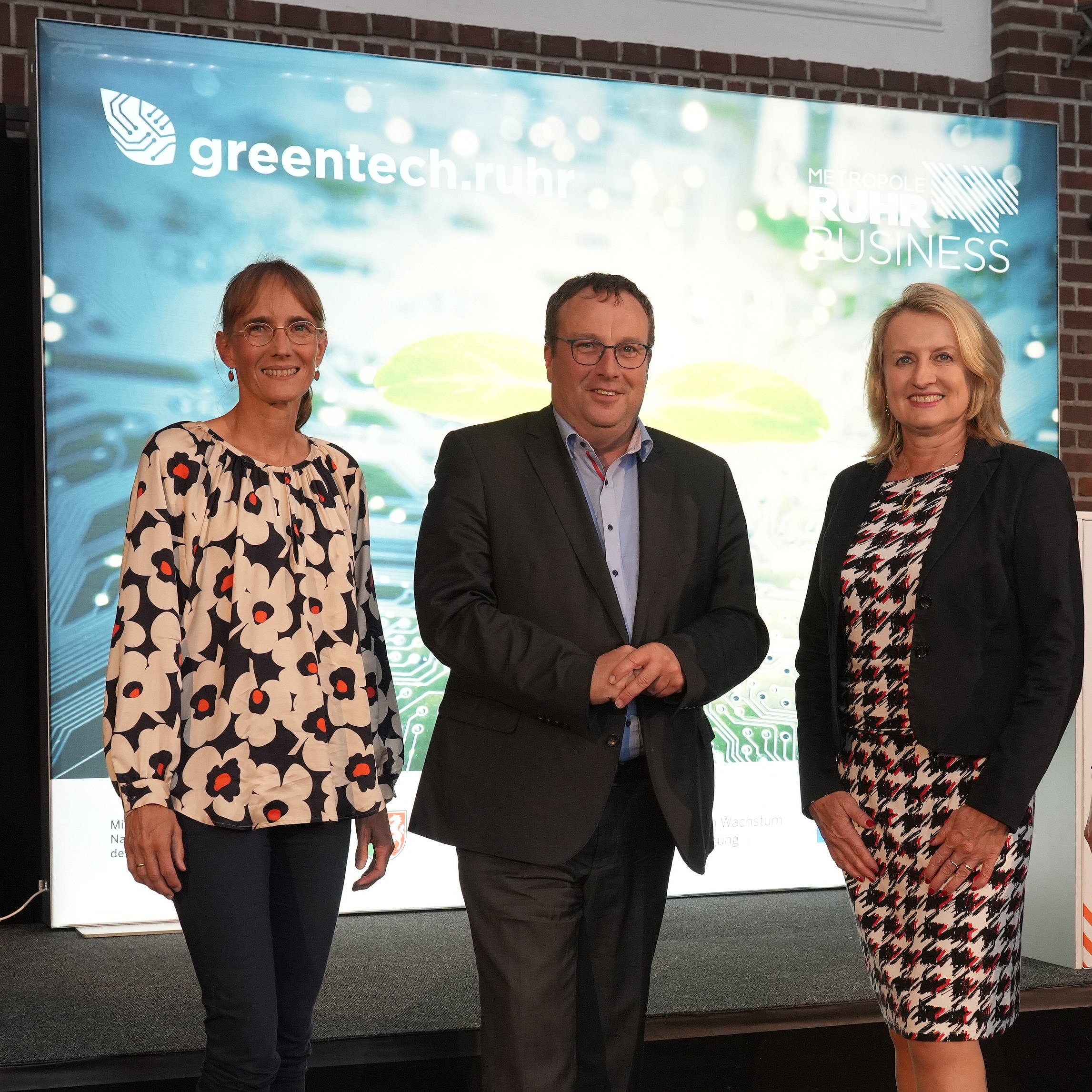Four people stand in front of a Greentech.Ruhr poster: Christina Zollmarsch, NRW Environment Minister Krischer, Prof. Dr. Julia Frohne and Alisa Schuler.