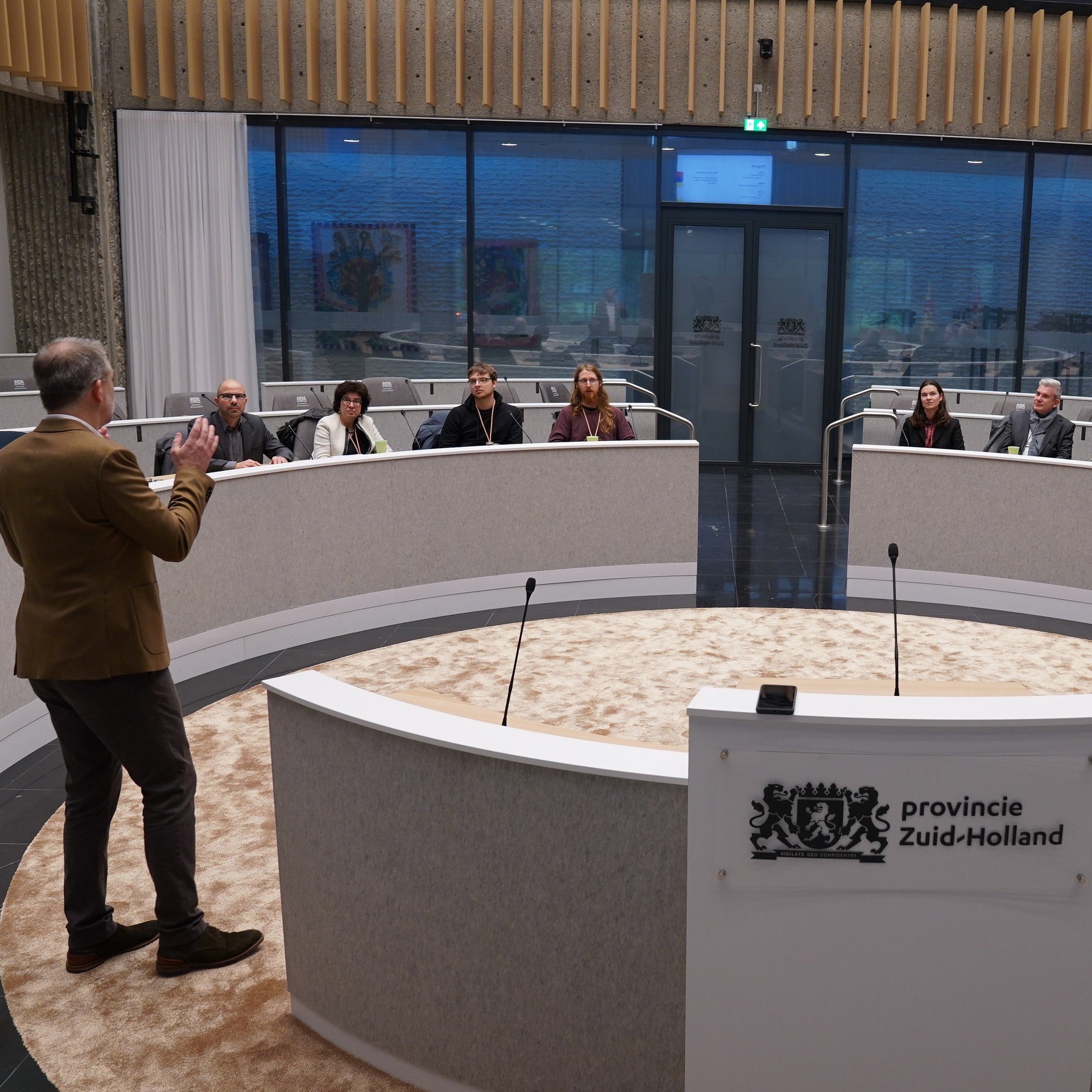Eine Gruppe sitzt im Parlament der Provinz Süd-Holland und ein Mann erklärt etwas.