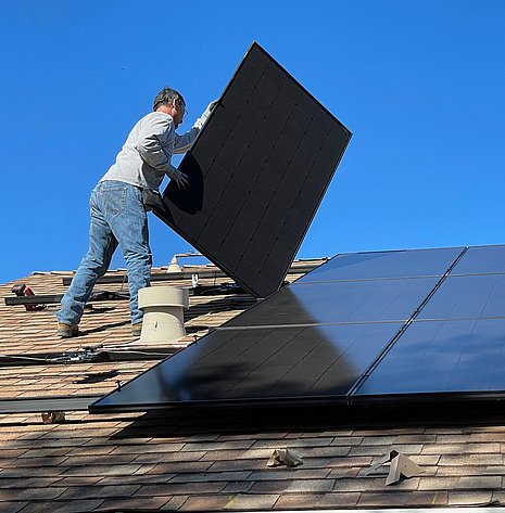 Abgebildet ist ein Moneur, der Solarpanelen auf einem Wohndach anbringt.