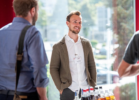 Auf einem Greentech.Ruhr-Netzwerktreffen stehen zwei Personen von hinten vor einer Person, die mittig zu einer Person lächelt.