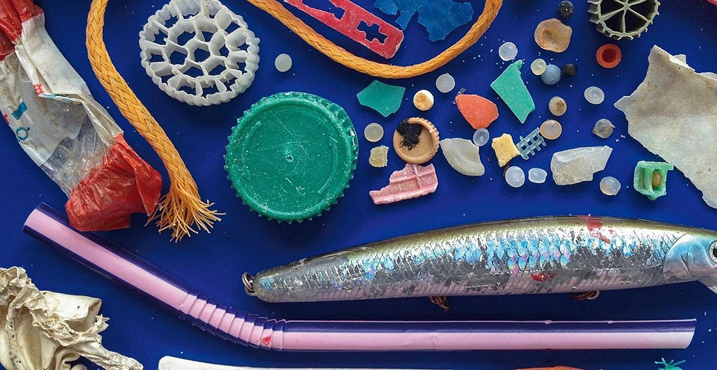 Blick aus der Vogelperspektive: Kleine Plastik-Gegenstände und Plastikmüll wie ein Trinkhalm, Flaschendeckel, Süßigkeitenverpackung und ein Fischköder liegen ordentlich gesammelt auf einer Fläche 